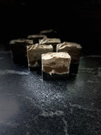 Four layered soap bars with dark brown and light beige swirls, arranged on a dark textured surface against a black background.